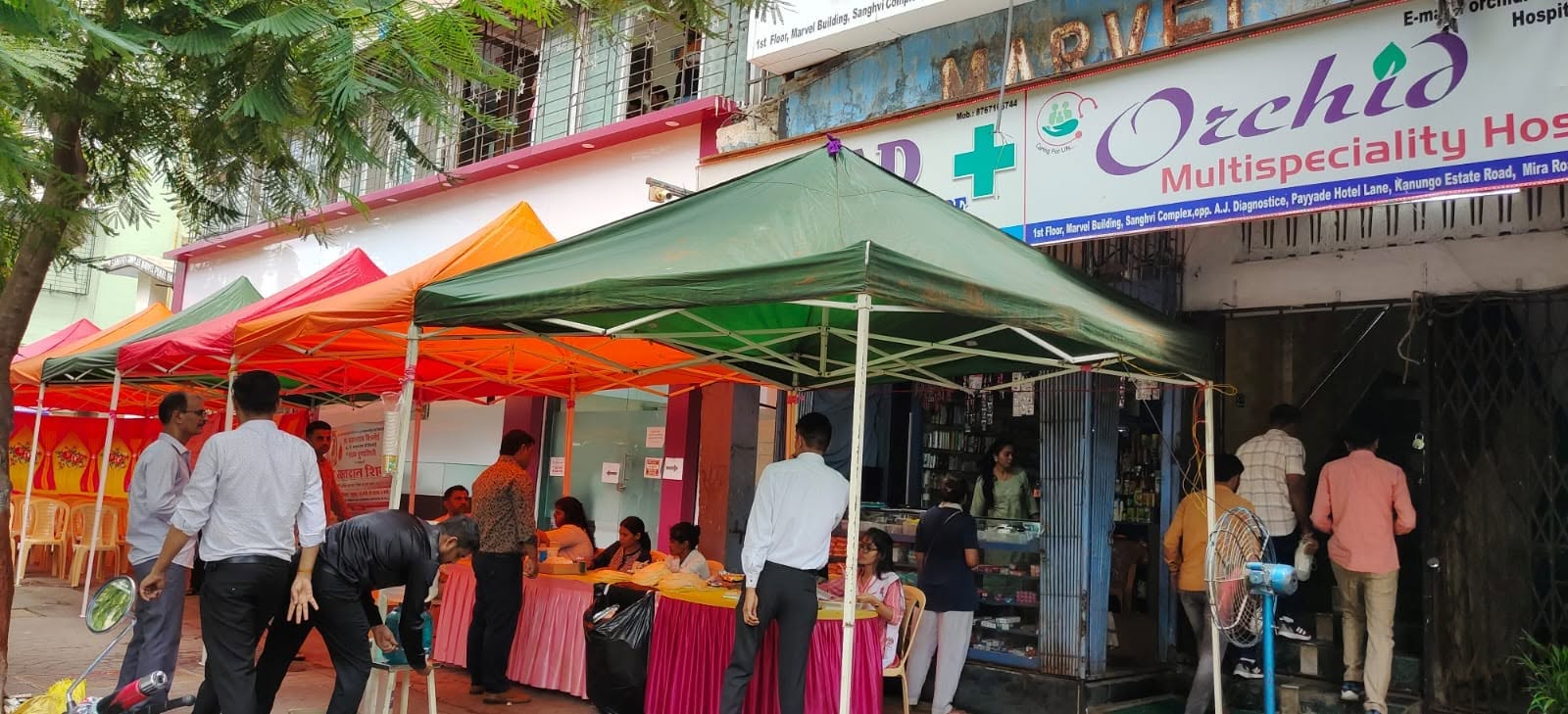The blood donation camp set up under canopies on the street outside Orchid Multispeciality Hospital, with the hospital signboard above.
