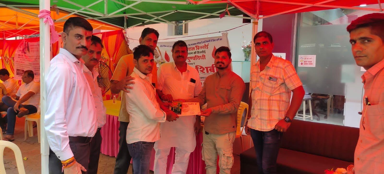A certificate is presented to a blood donor while other volunteers look on from around the camp table.