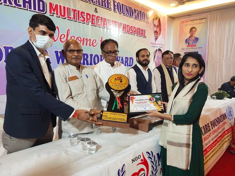 Two attendees hold a Corona Warrior Award trophy and certificate between them at the Maxwin Humancare Foundation and Orchid Multispeciality Hospital award ceremony.