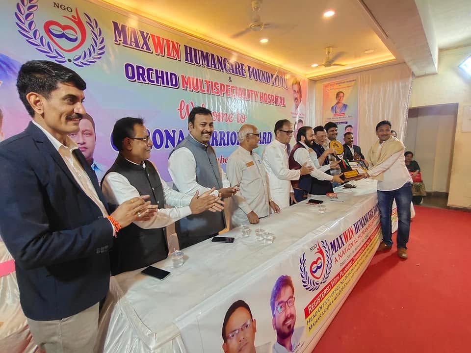 A recipient accepts a trophy at the head table while a row of guests applauds, under the Maxwin Humancare Foundation and Orchid Multispeciality Hospital banner.