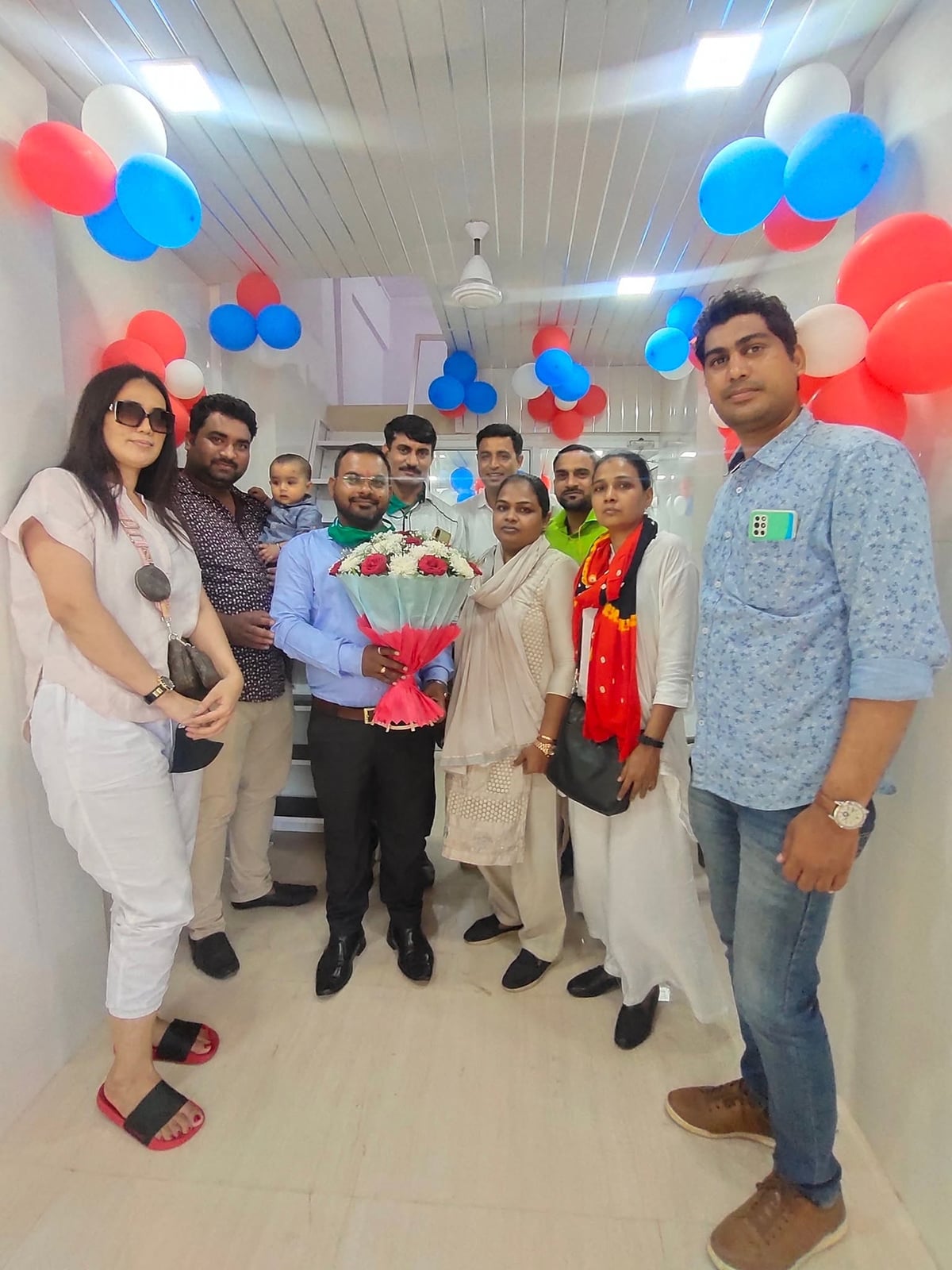 Hospital staff and family members gather with a bouquet inside a newly fitted, balloon-decorated corridor on opening day.