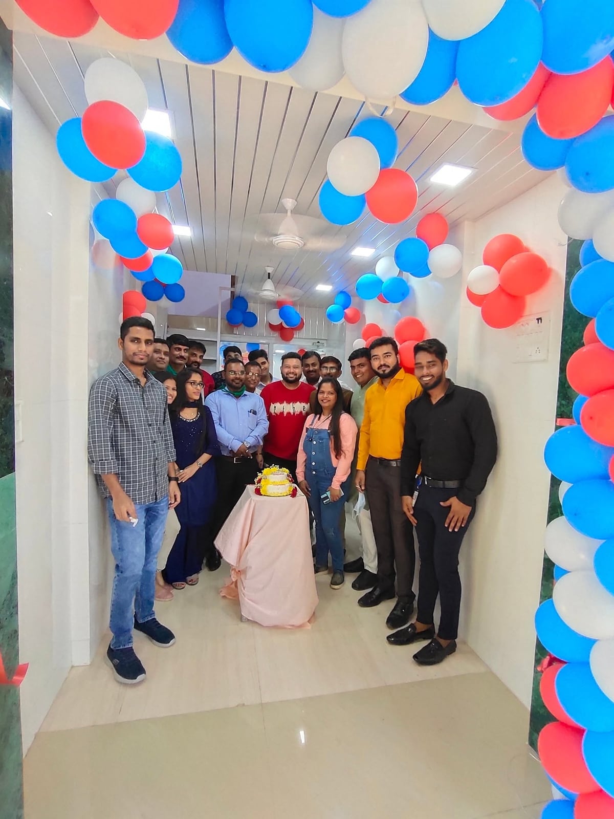 The hospital team stands around a tiered cake in a corridor decorated with red, white and blue balloons.