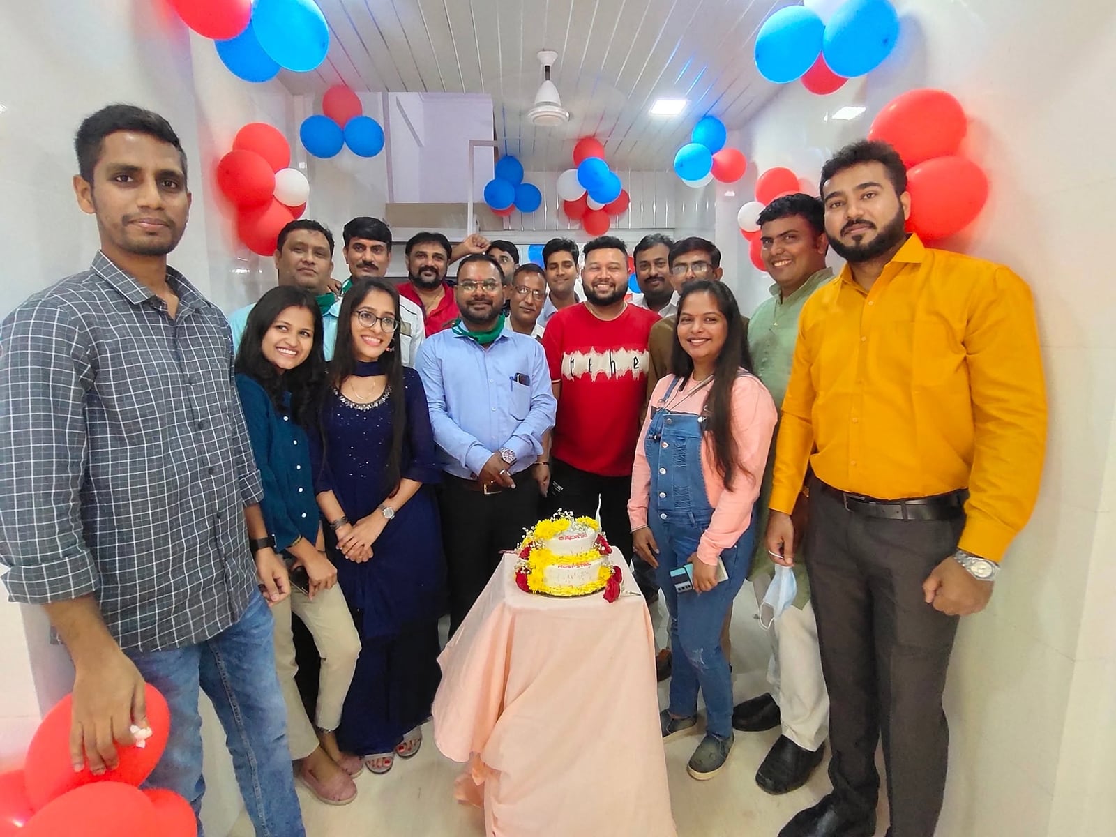 A large group of hospital staff poses behind a celebration cake iced with the Orchid Multispeciality Hospital name.